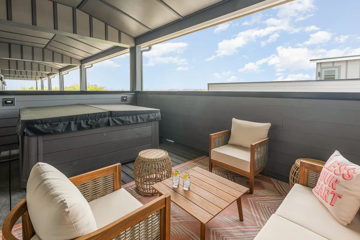 A cozy, tranquil outdoor area with a hot tub, stylish lounge seating adorned with decorative pillows, and a coffee table, all set against a backdrop suitable for both morning relaxation and evening gatherings. The ambiance is serene and ideal for intimate groups.