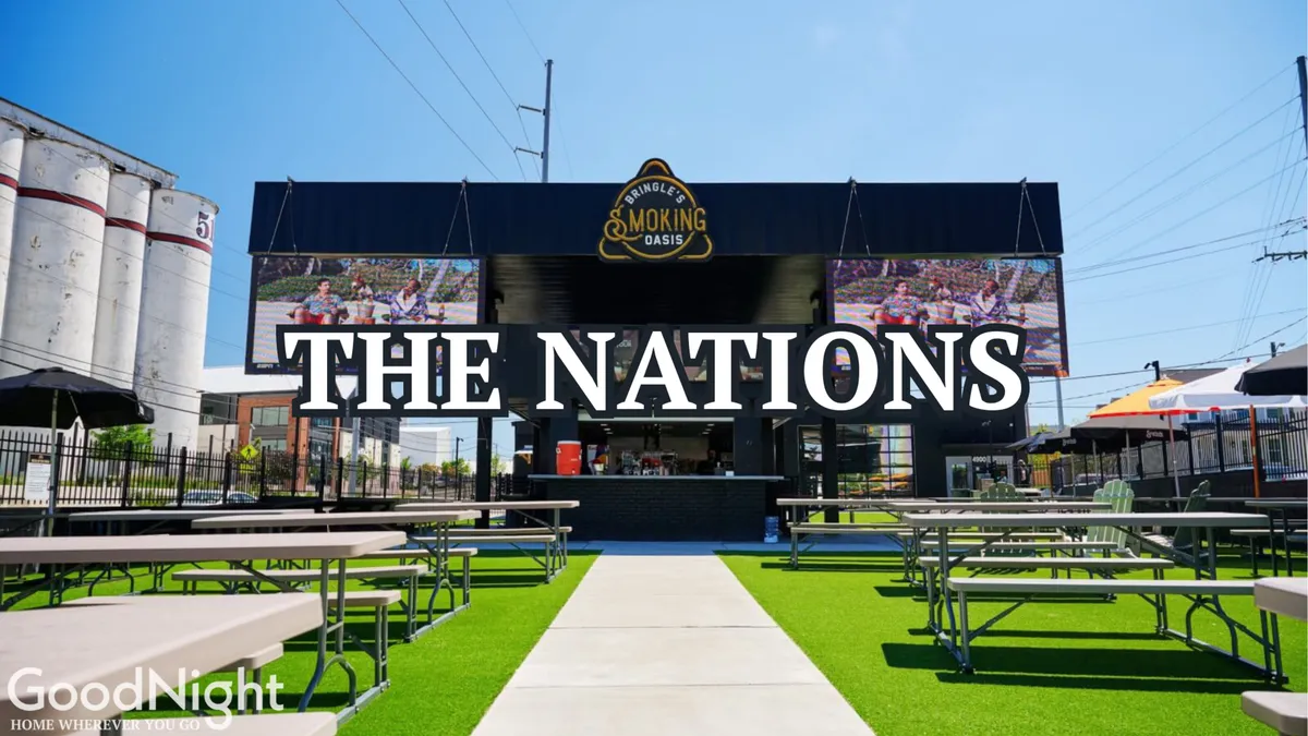 An exterior space featuring large signage reading 'THE NATIONS', a smoking oasis structure, and a festive outdoor seating area. The setting is equipped for live music and social gatherings, suggesting a community-driven atmosphere with open-air entertainment.