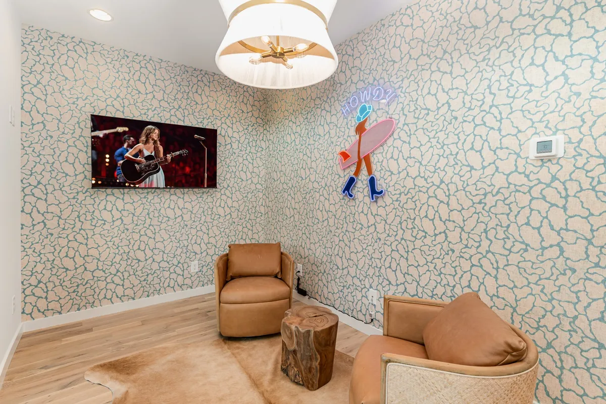 This image shows a stylish living area with bold artwork, a playful neon sign, comfortable chairs, and a wooden coffee table. The atmosphere is casual and energetic, perfect for after-hours hangouts or socializing after a night out.