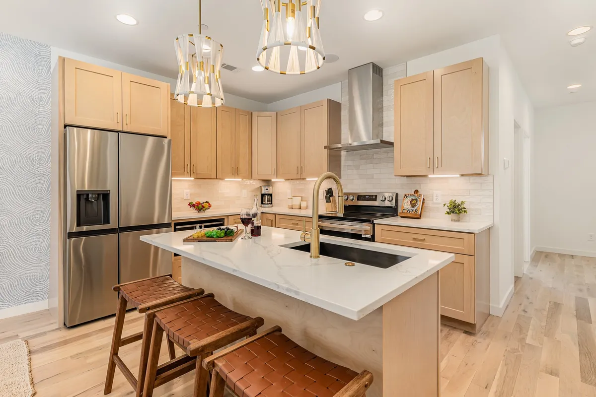 A contemporary kitchen featuring a spacious island with bar seating, gleaming stainless steel appliances, and stylish decorative lighting. The setup is open and inviting, designed for both cooking and socializing, with ample counter space ideal for meal prep and group gatherings.