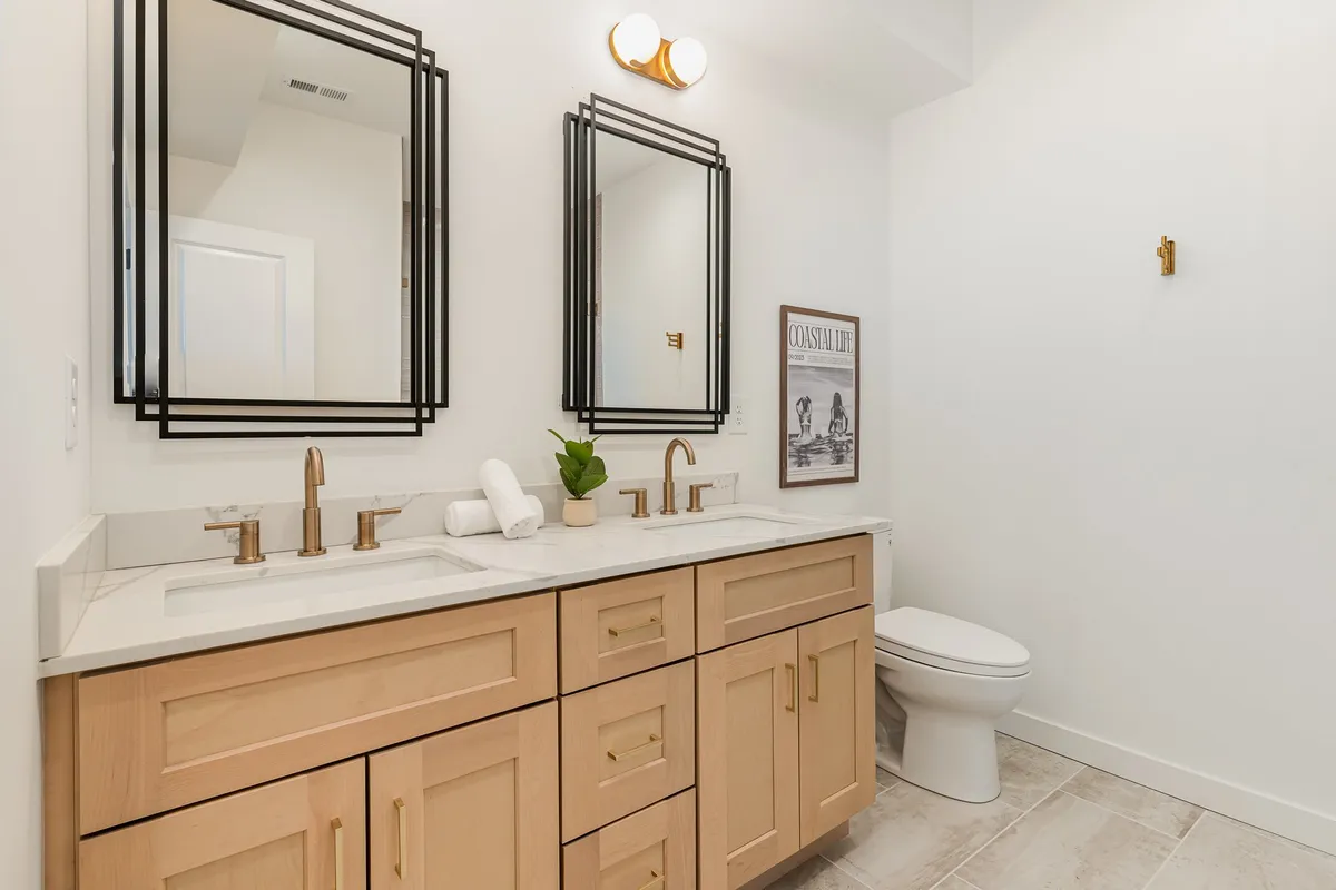 A spacious, spa-inspired bathroom featuring dual sinks, large mirrors, a stylish vanity, and framed artwork. The clean lines and fresh decor evoke a sense of luxury and tranquility, perfect for self-care routines.