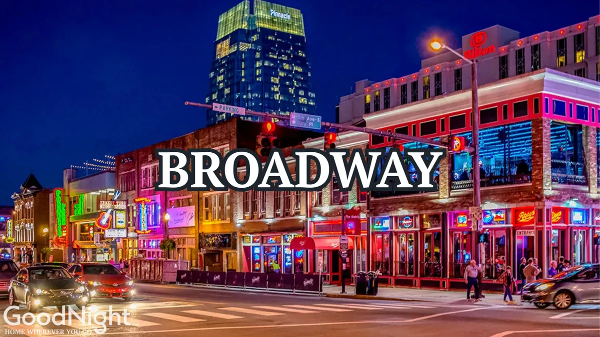 A lively Nashville street at night illuminated by neon signs and building lights, with people walking, traffic lights shining, and a bustling urban vibe. The scene captures the energy and vibrancy of downtown nightlife, evoking the excitement of exploring live music venues and bars near Broadway.